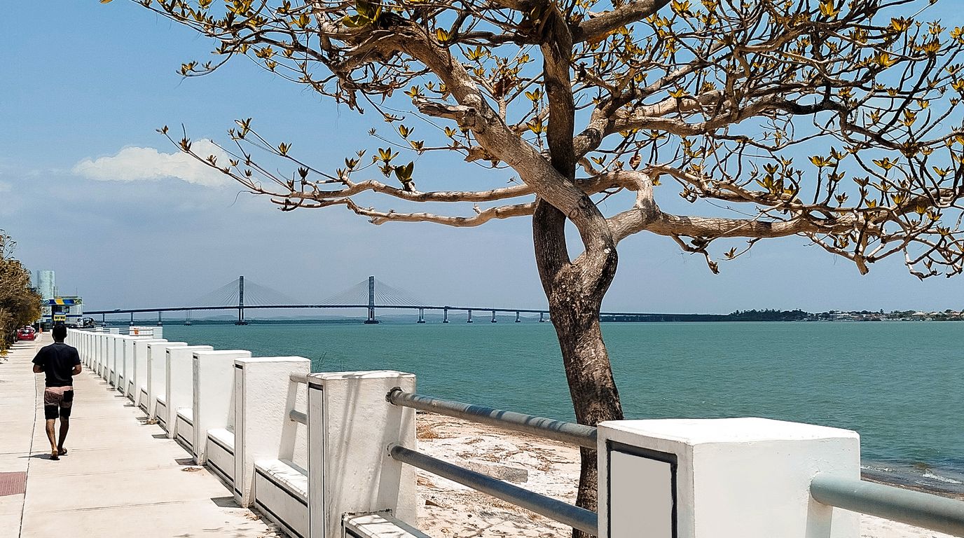 Orla à beira do rio com passeio calçado e ponte estaiada ao fundo.