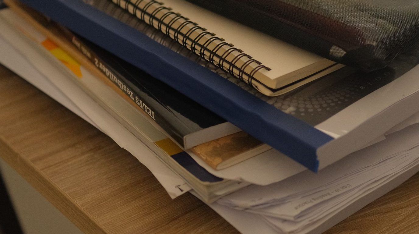 Livros e cadernos empilhados sobre uma mesa de estudo.